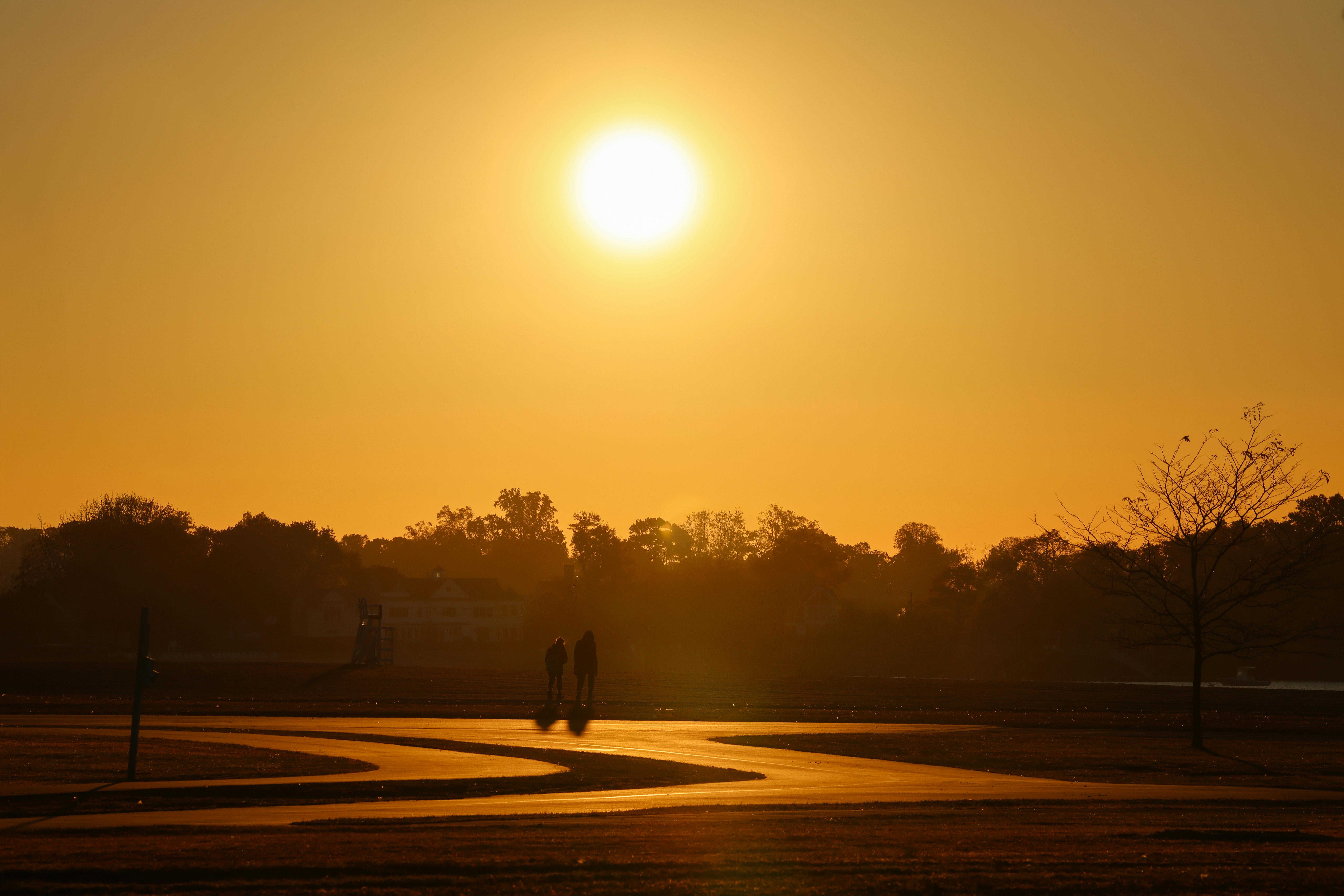 imagen de dos personas caminando por un paseo con el atardecer de fondo